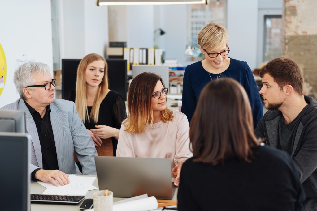 Dedicated business team having a brainstorming session or meeting gathered around a young woman with a laptop having a serious discussion