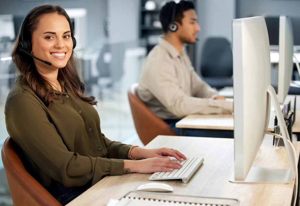 Woman typing at computer, call center and contact us with communication and CRM with tech support. Customer service, help desk and telemarketing, female consultant and smile in portrait with telecom.