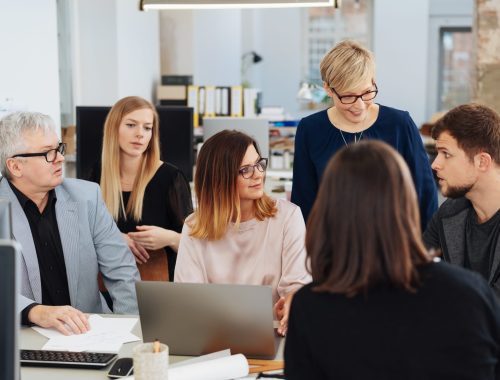 Dedicated business team having a brainstorming session or meeting gathered around a young woman with a laptop having a serious discussion